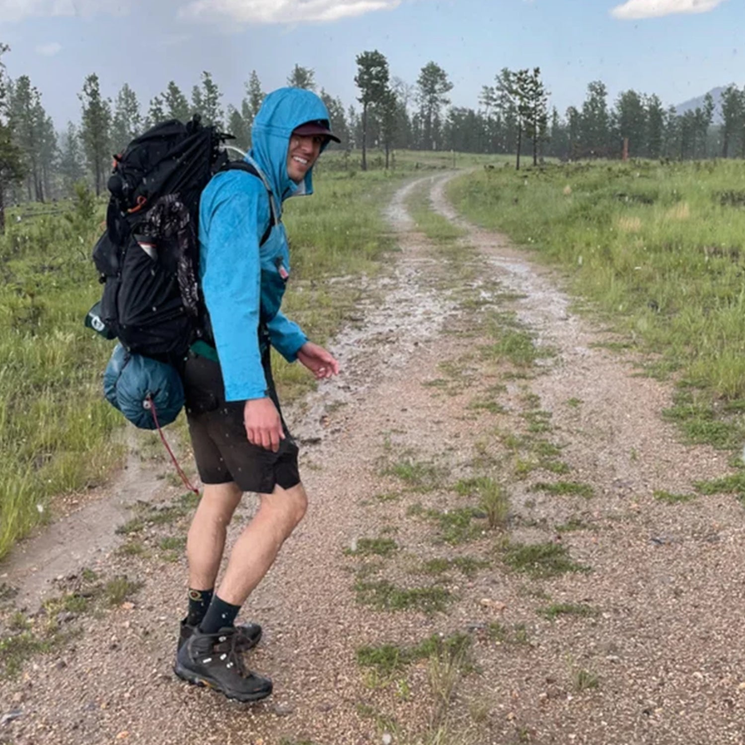 Hiker in blue raincoat smiles while hiking through the rain