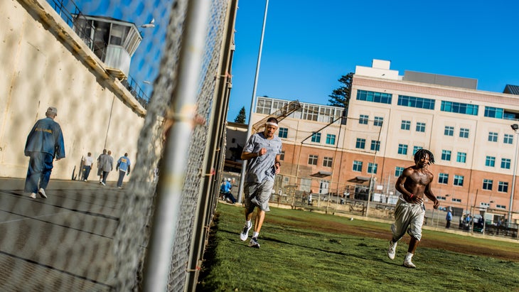 A man runs in a grey shirt in prison in front of a blue sky.