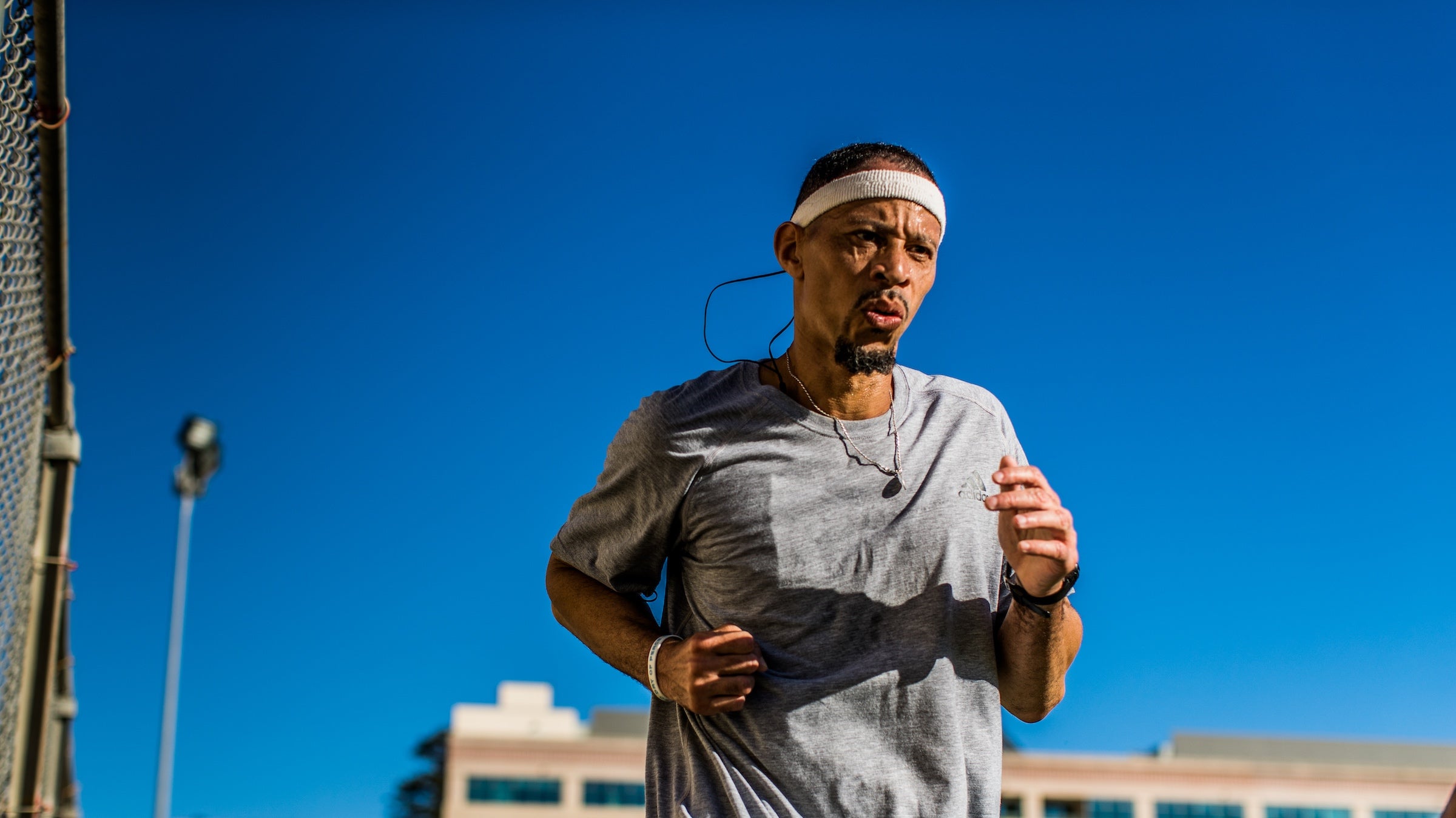 A man runs in a grey shirt in prison in front of a blue sky.