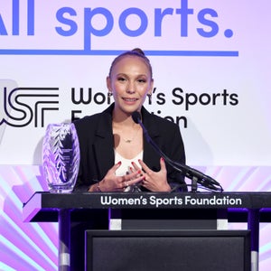 A woman accepts an award on a stage with a black blazer on