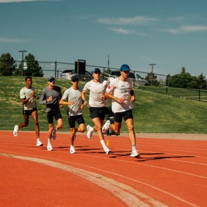 guys running on a red track in white shoes