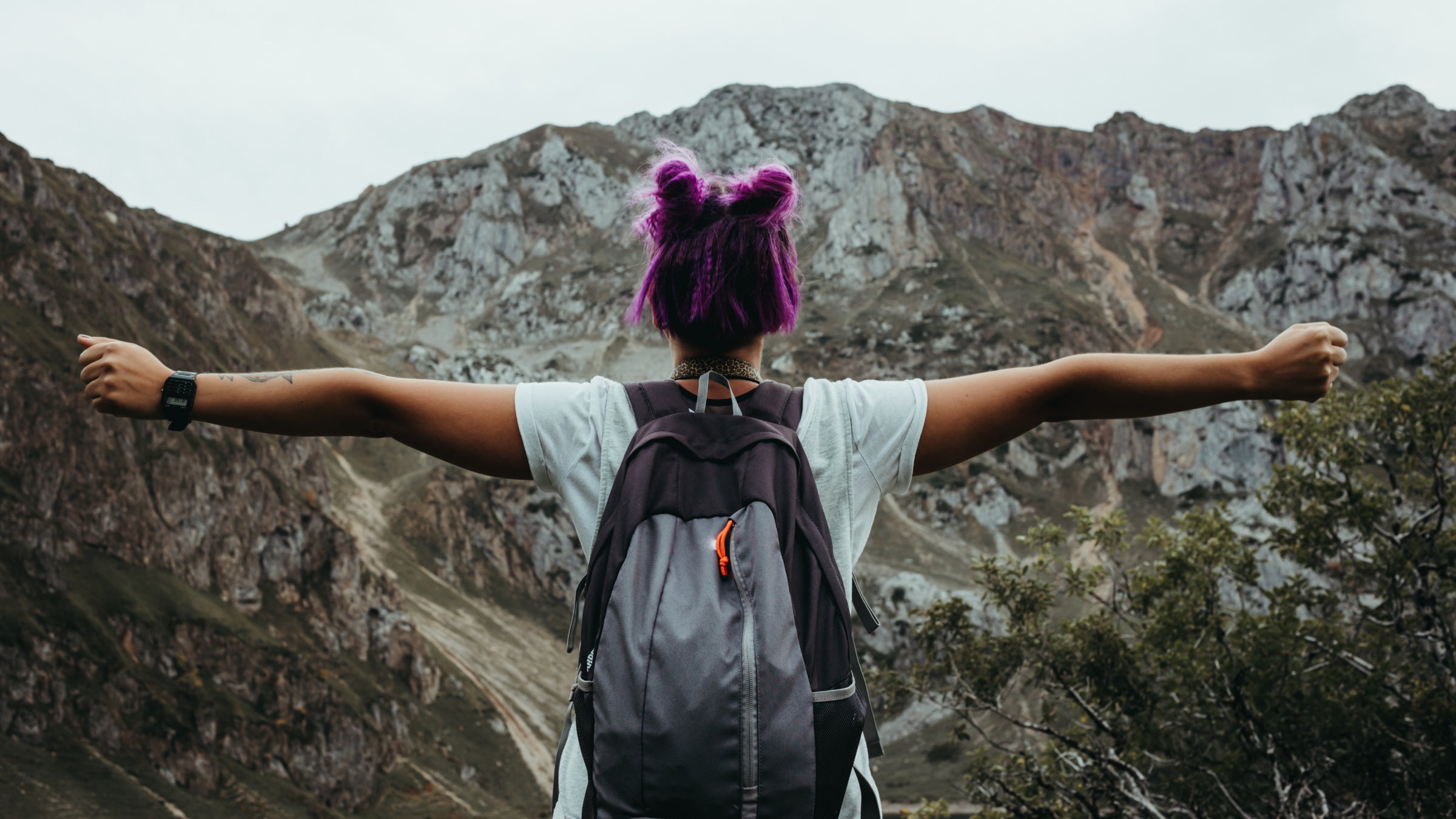 woman of color with purple hair with outstretched arms while hiking