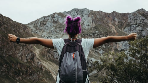 woman of color with purple hair with outstretched arms while hiking