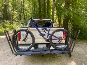 Kuat Piston Pro bike rack carrying a mountain bike mounted to the back of a white pickup truck.
