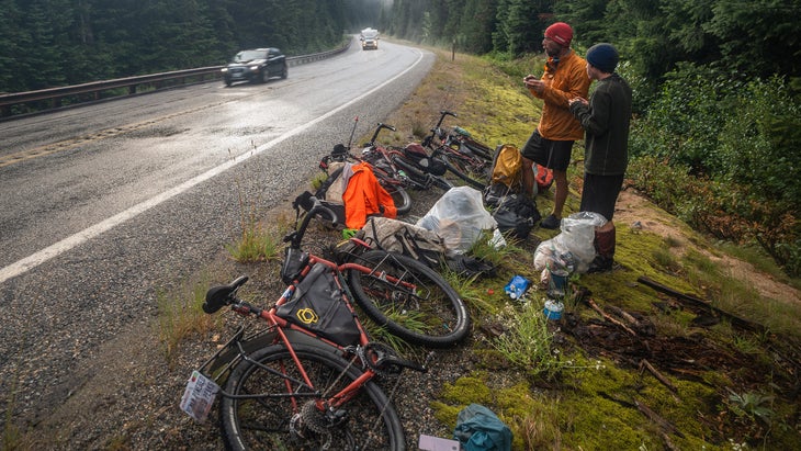 Two cyclists stand by their bicycles on the side of the road.