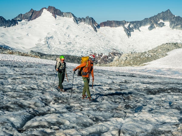 Two climbers walk below a soaring glacier.