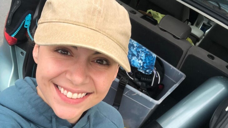 The author wearing a ball cap and, behind her, a dive tank, a wetsuit, and other scuba gera