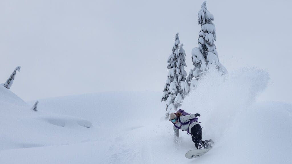 A snowboarding ripping a line down a slope in the backcountry of British Columbia