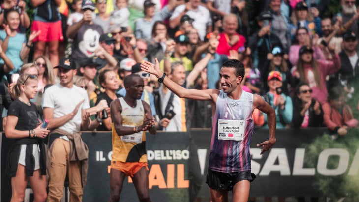 A man finishes a race with a white shirt on and a background of spectators.