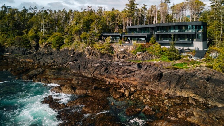 An exterior view of The Nami Project, set against the cedar trees of a rainforest, with waves crashing against the rocky shoreline