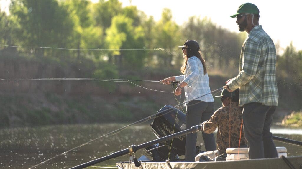 A man and a woman cast their fly rods into the river while a guide navigates the small boat.