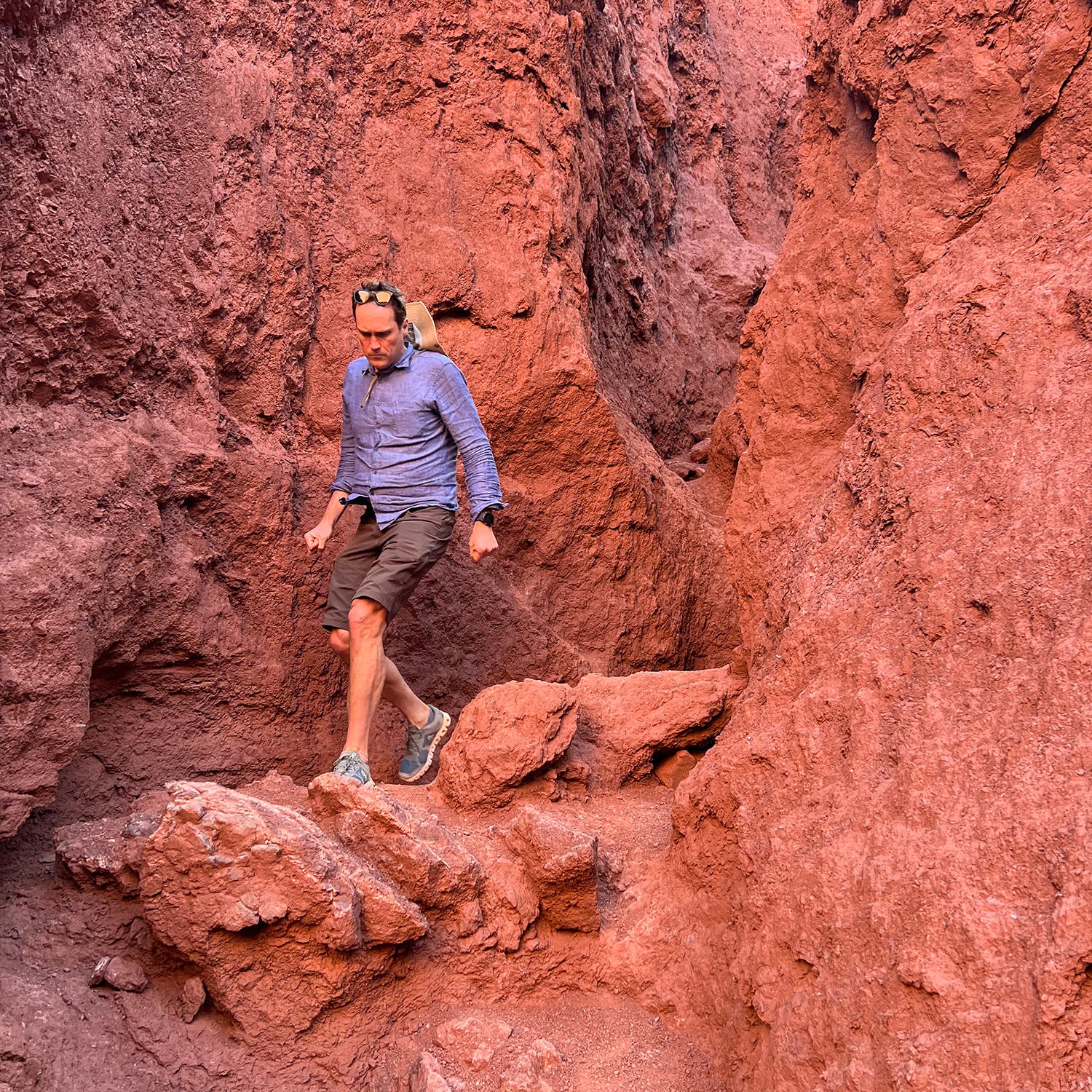 A man in hiking clothes walks through a slot canyon with red walls