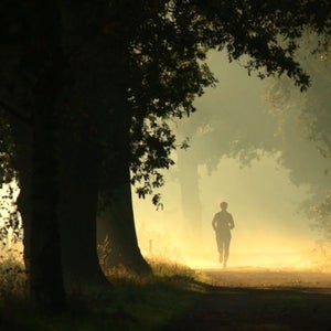 A woman runs on a misty trail in the forest at dawn
