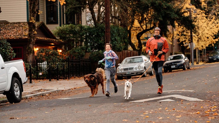 A father and his father run down the road with dogs.