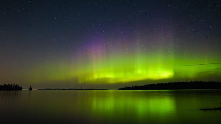 A display of bright yellow, green and pink northern lights above the horizon of Lake Superior