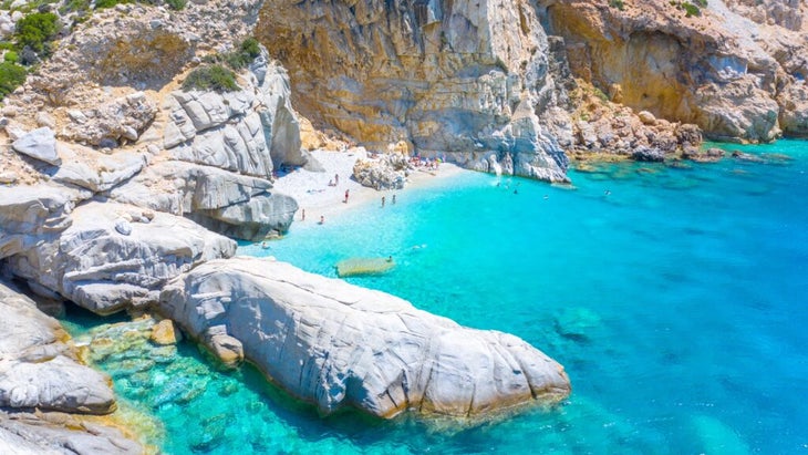 beach-goers wade into an impossibly turquoise inlet on the island of Ikaria
