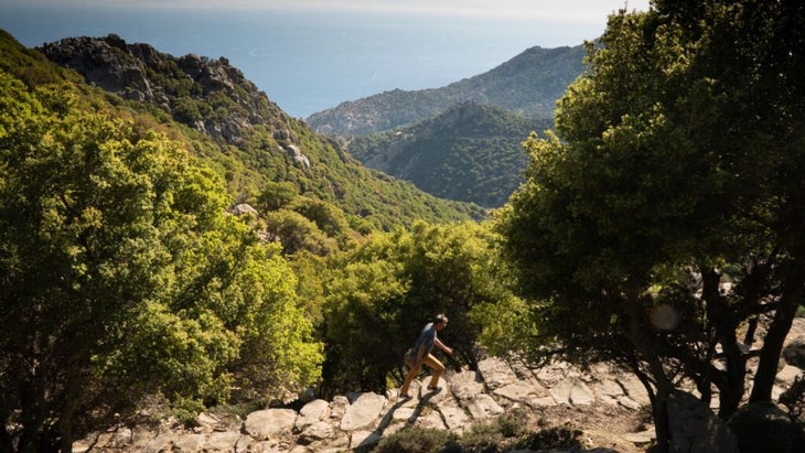Buettner hiking up a trail in Ikaria with green hillsides tumbling down to the sea