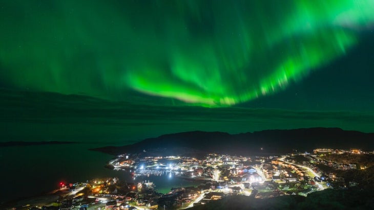 Swirls of green northern lights above the waterfront town of Qaqortoq, Greenland