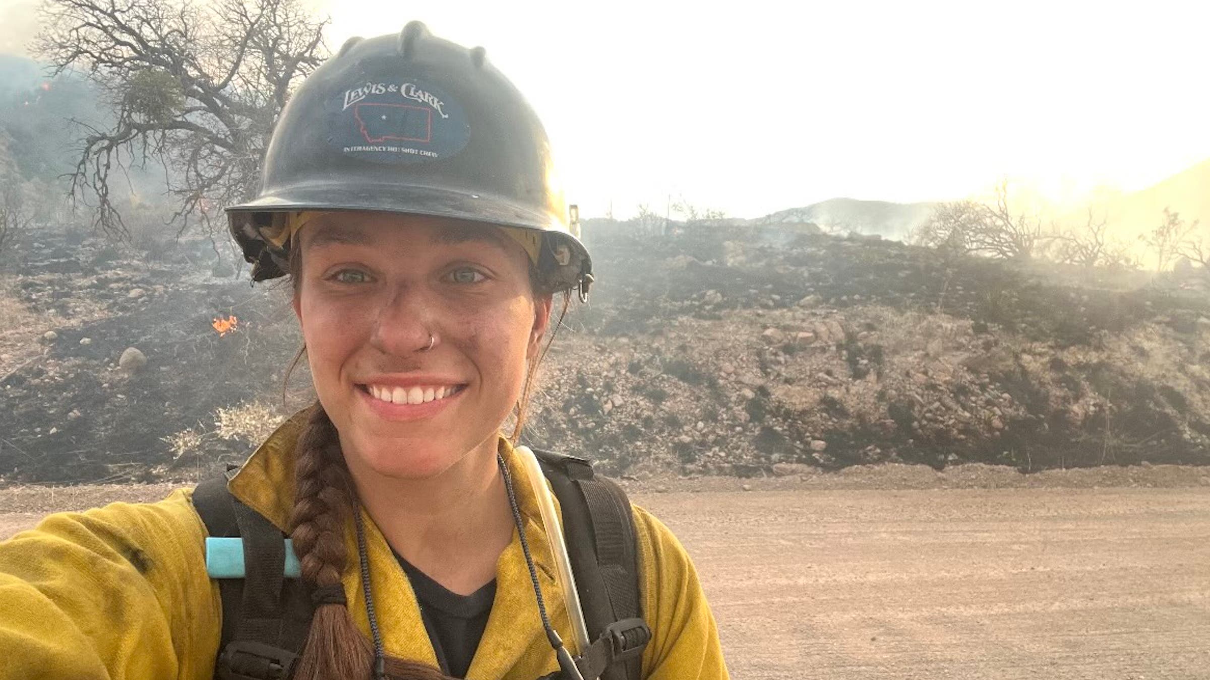 A woman smiles on duty in a yellow firefighter suit.
