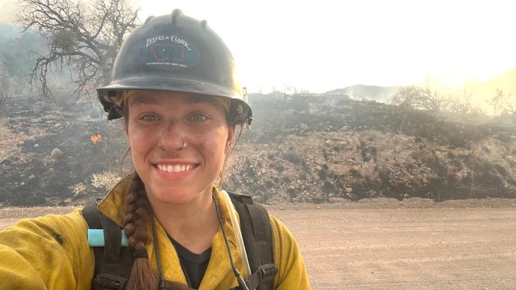 A woman smiles on duty in a yellow firefighter suit.