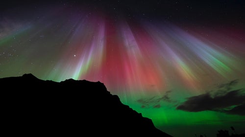 Rays of vibrantly colored northern lights shooting down from the sky and reflecting off a body of water