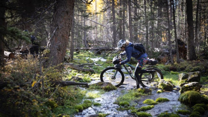 Stephanie Pearson walking her mountain bike across a shallow streamed on Utah’s Great Western Trail