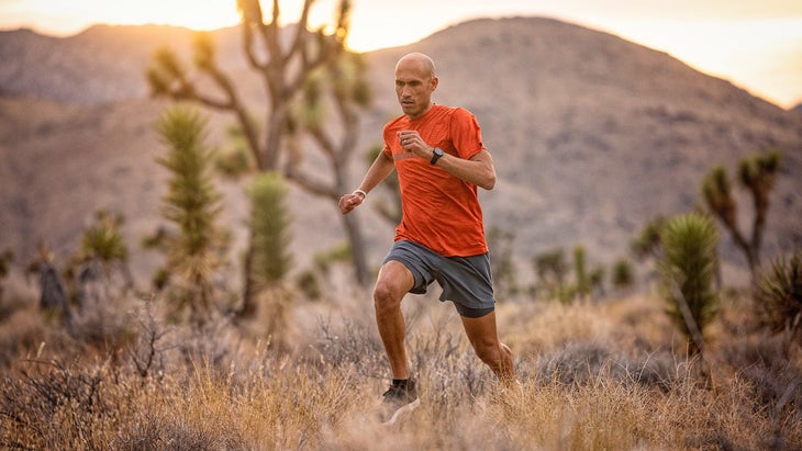 A man in an orange shirt runs in the desert