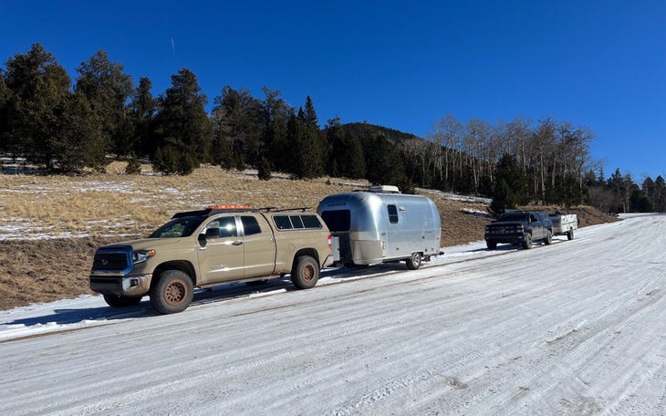 Truck with Airstream trailer attached parked on snowy winter road.