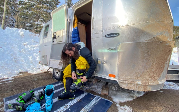 Man putting on ski boots on stoop of Airstream trailer. 