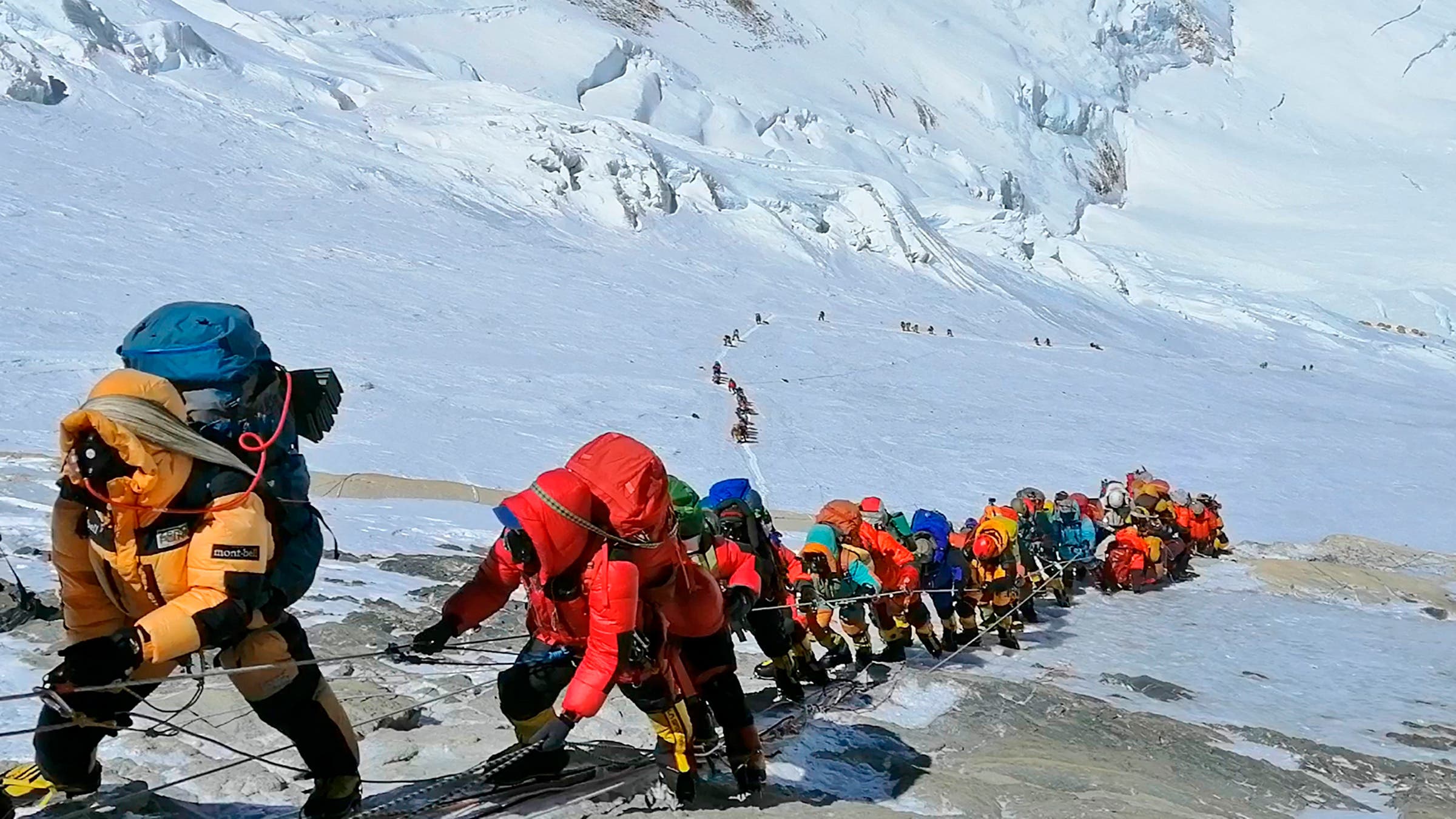A line of mountaineers climbs Mount Everest.