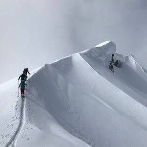 Three skiers ascend a snow-covered, corniced ridge
