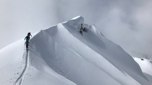 Three skiers ascend a snow-covered, corniced ridge