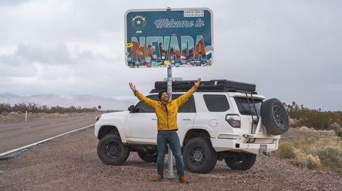 Creator Jacob Moon in front of the Welcome to Nevada sign on a Southern Nevada road trip