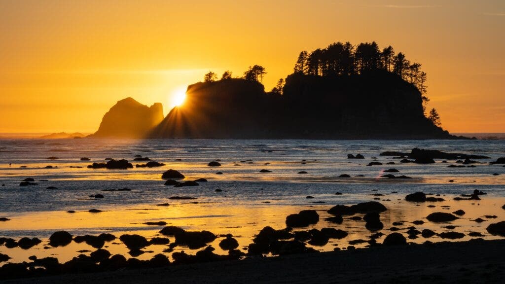 The sun sets over a forested island off Cape Alava, Washington.