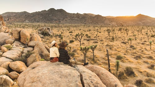 Two women sitting atop huge boulders, watching the sunset at Joshua Tree National Park, California.
