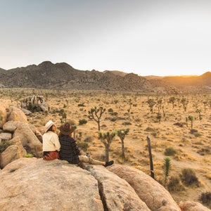 Two women sitting atop huge boulders, watching the sunset at Joshua Tree National Park, California.