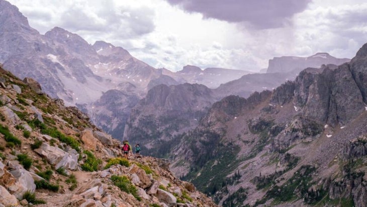 Two hikers climbing atop a steep mountain in Wyoming’s Grand Tetons.