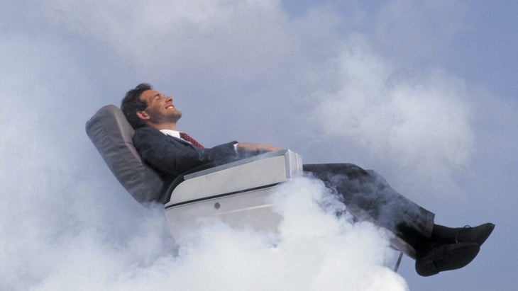 A smiling man reclines comfortably in his airplane seat, surrounded by clouds, as if in a dream.