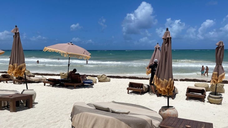 A white-sand beach is adorned with beach chairs and umbrellas in Tulum, Mexico.