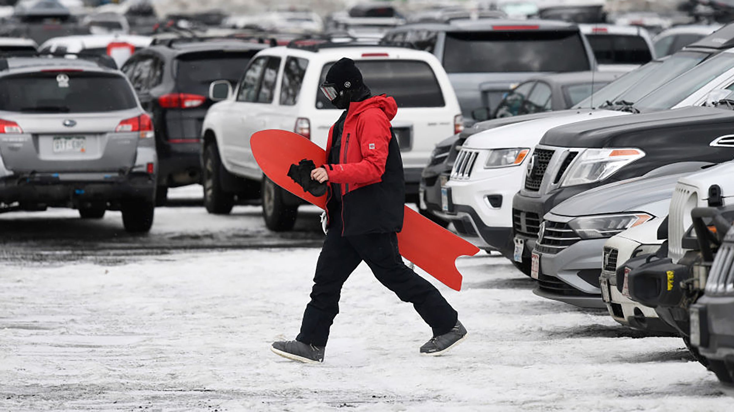 A snowboarder walks across a crowded parking lot