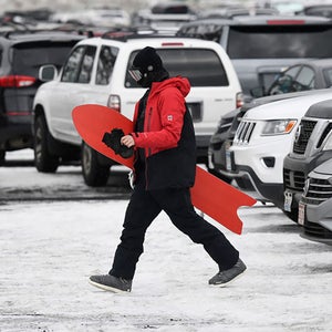 A snowboarder walks across a crowded parking lot