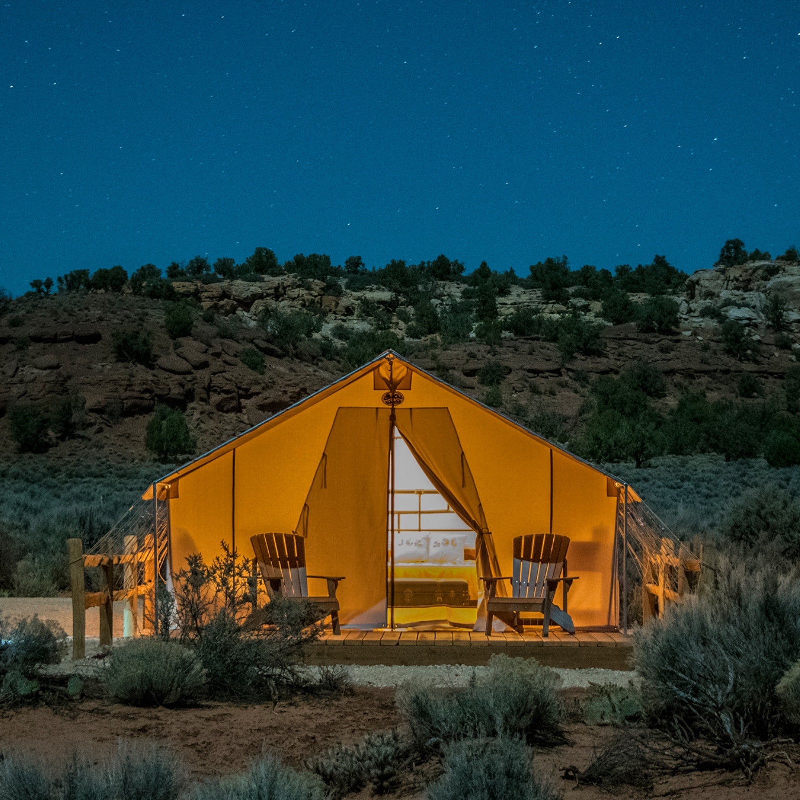 A glowing tent with two camp chairs out front sets a cozy scene amid southwestern Utah's desert.