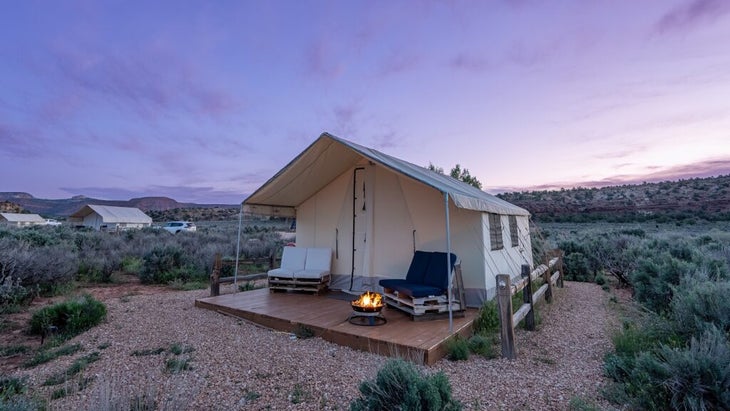A BaseCamp 37 glamping tent with two chairs and a grill fire out front sets a cozy scene amid the southwestern desert landscape near Kanab, Utah.