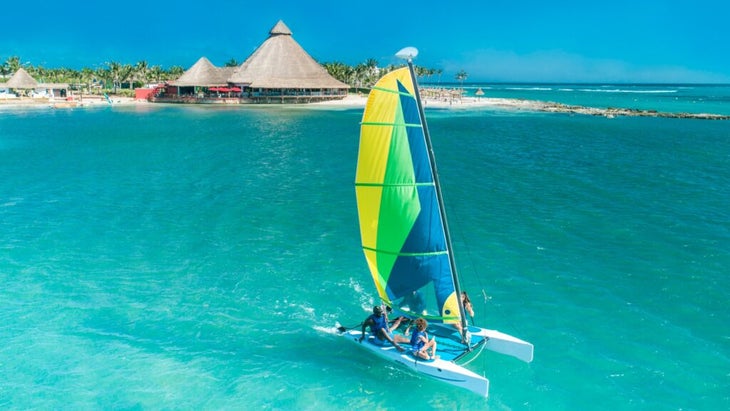 A family of four on a catamaran cruises away from the Caribbean shoreline of Mexico and into deeper turquoise waters. 