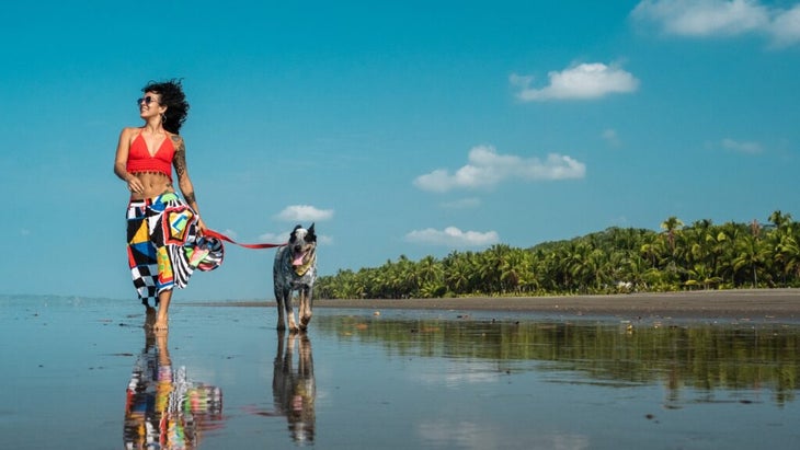 A woman walks her dog on a Costa Rican beach.