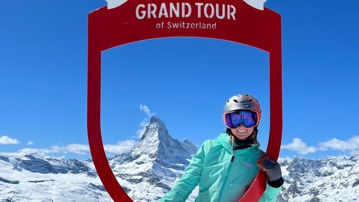 The author poses at a sign that says "Grand Tour of Switzerland," with a view of the Matterhorn behind her.