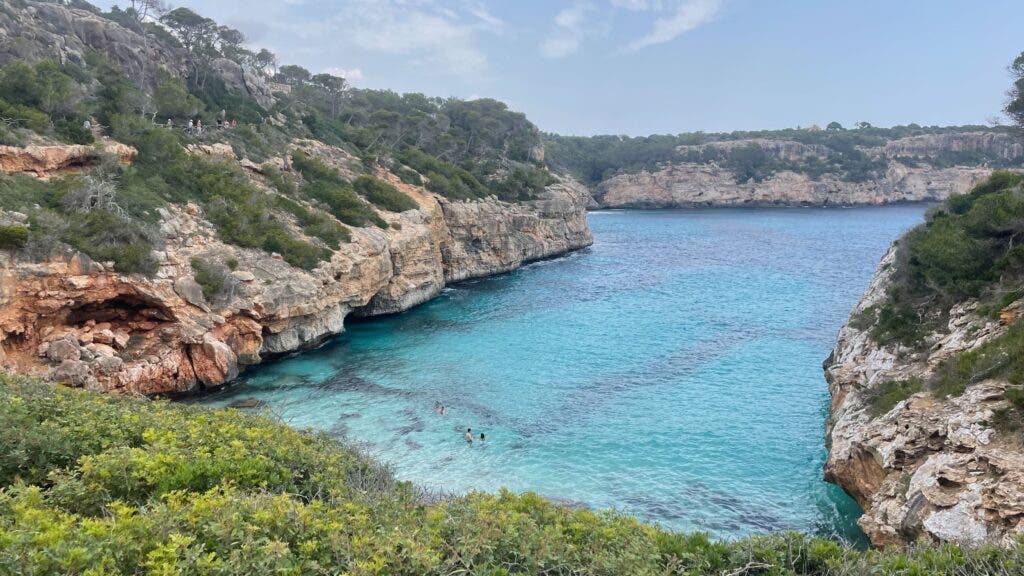 A turquoise cove of Majorca, Spain, where a few swimmers are enjoying a dip.