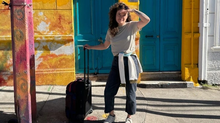 The author outside some colorful buildings in Valparaíso, Chile, holding on to her suitcase handle.