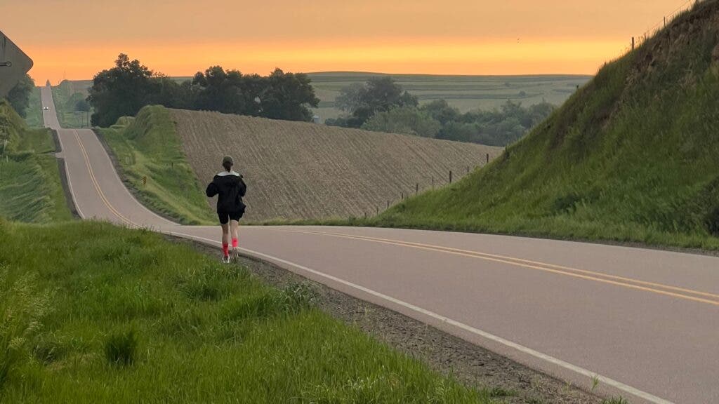 A woman running on a country road near a field at sunset