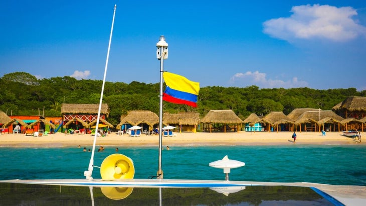 A boat waving the Colombian flag prepares to pull up to the sandy shore of the Rosario Islands.
